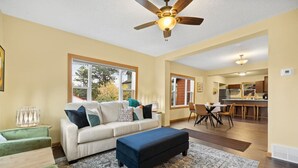 A living room with a sofa, ottoman, and a ceiling fan. There is a dining area with a table and chairs. - JoLee Pines, Close to attractions (Lead)