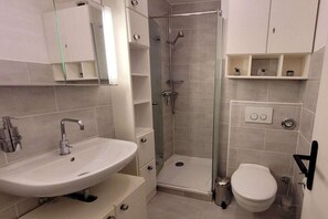A bathroom with a sink, toilet, shower, and storage cabinets.