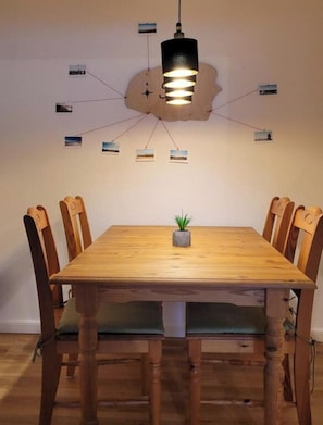 A dining table with chairs, a hanging light fixture, and a wall-mounted clock.