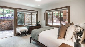 Un dormitorio con una cama grande, un escritorio y una silla, con pared de piedra y ventanas.