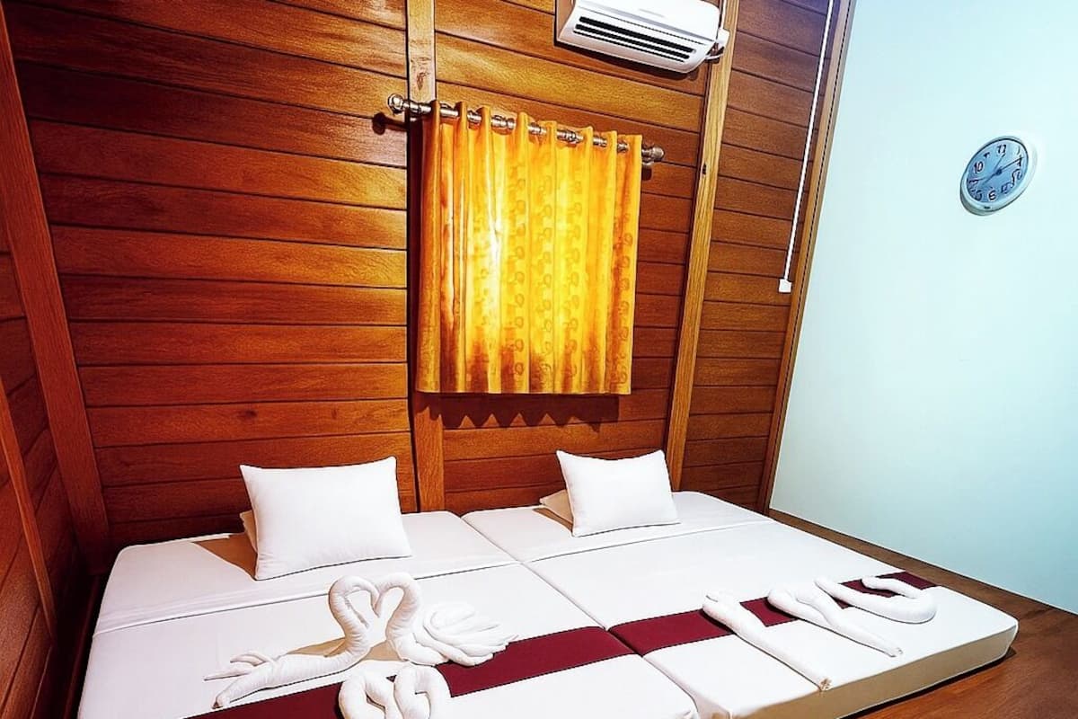 A wooden-paneled room with a bed, an air conditioning unit, and a clock on the wall.
