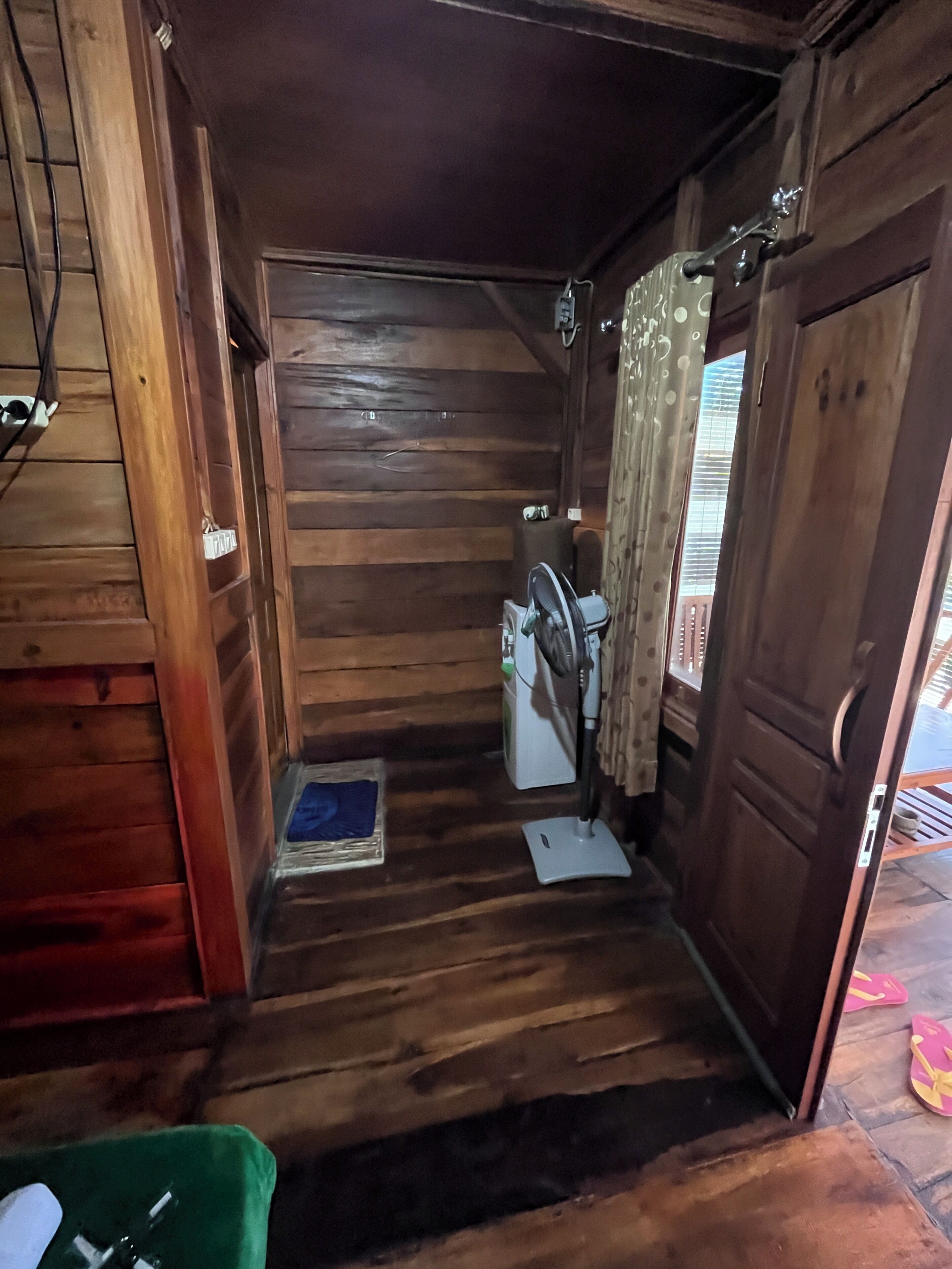 Interior d'una cabana de fusta amb rentadora, un ventilador i una petita catifa al terra.