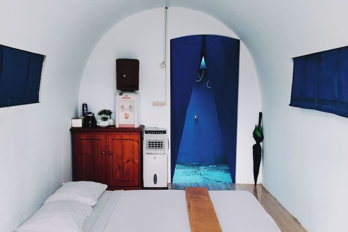 A bedroom with a bed, a wooden wardrobe, a white heater, and a blue curtain.