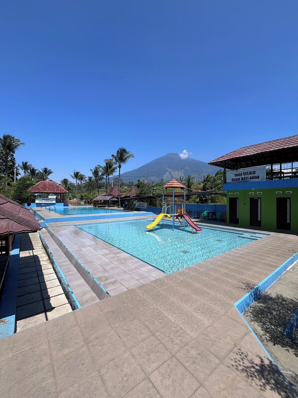 Ein Pool mit Rutsche und Kinderspielbereich, umgeben von Palmen und einem Berg im Hintergrund.