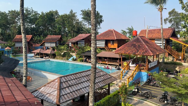 A resort with a swimming pool, wooden bungalows, and a parking area with motorcycles. - Pondok Cilega (Mandirancan)