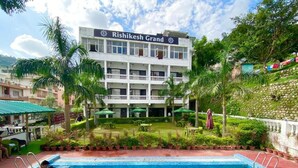 A swimming pool with a building labeled "Rishikesh Grand" in the background. - Hotel Rishikesh Grand by Kool-stays (Rishikesh)