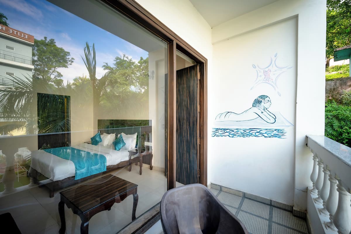 Un balcón con puerta de cristal que da a un dormitorio con cama, una mesita y vista a una piscina.