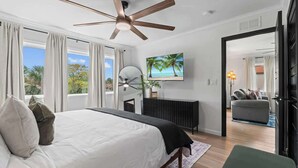 A bedroom with a bed, ceiling fan, TV, and a view of the outdoors. - Palms at Arricola B - Team Joseph Ellen (St. Augustine)
