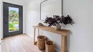 A modern entryway with a wooden console table, a mirror, and wicker baskets. - Palms at Arricola B - Team Joseph Ellen (St. Augustine)