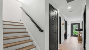 A staircase with wooden steps and a black handrail, a hallway with a black door, and a wooden floor. - Palms at Arricola B - Team Joseph Ellen (St. Augustine)