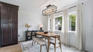 A dining area with a wooden table, chairs, a bench, a chandelier, and a view through large windows. - Palms at Arricola B - Team Joseph Ellen (St. Augustine)