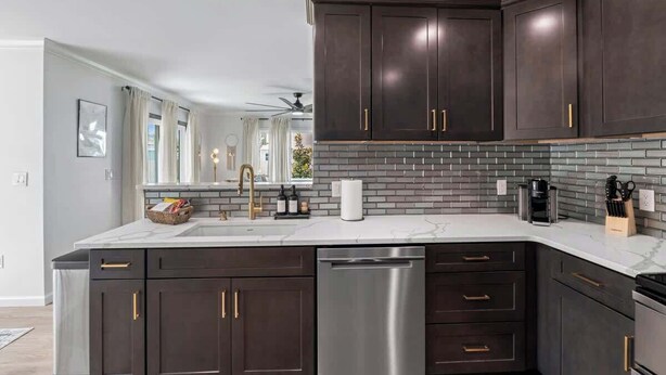 A modern kitchen with dark cabinetry, a stainless steel dishwasher, and a tiled backsplash. - Palms at Arricola B - Team Joseph Ellen (St. Augustine)