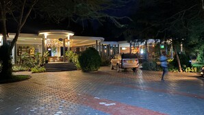 Ein gut beleuchteter Hotel Eingangsbereich mit überdachter Außenbestuhlung und einem gepflasterten Weg.