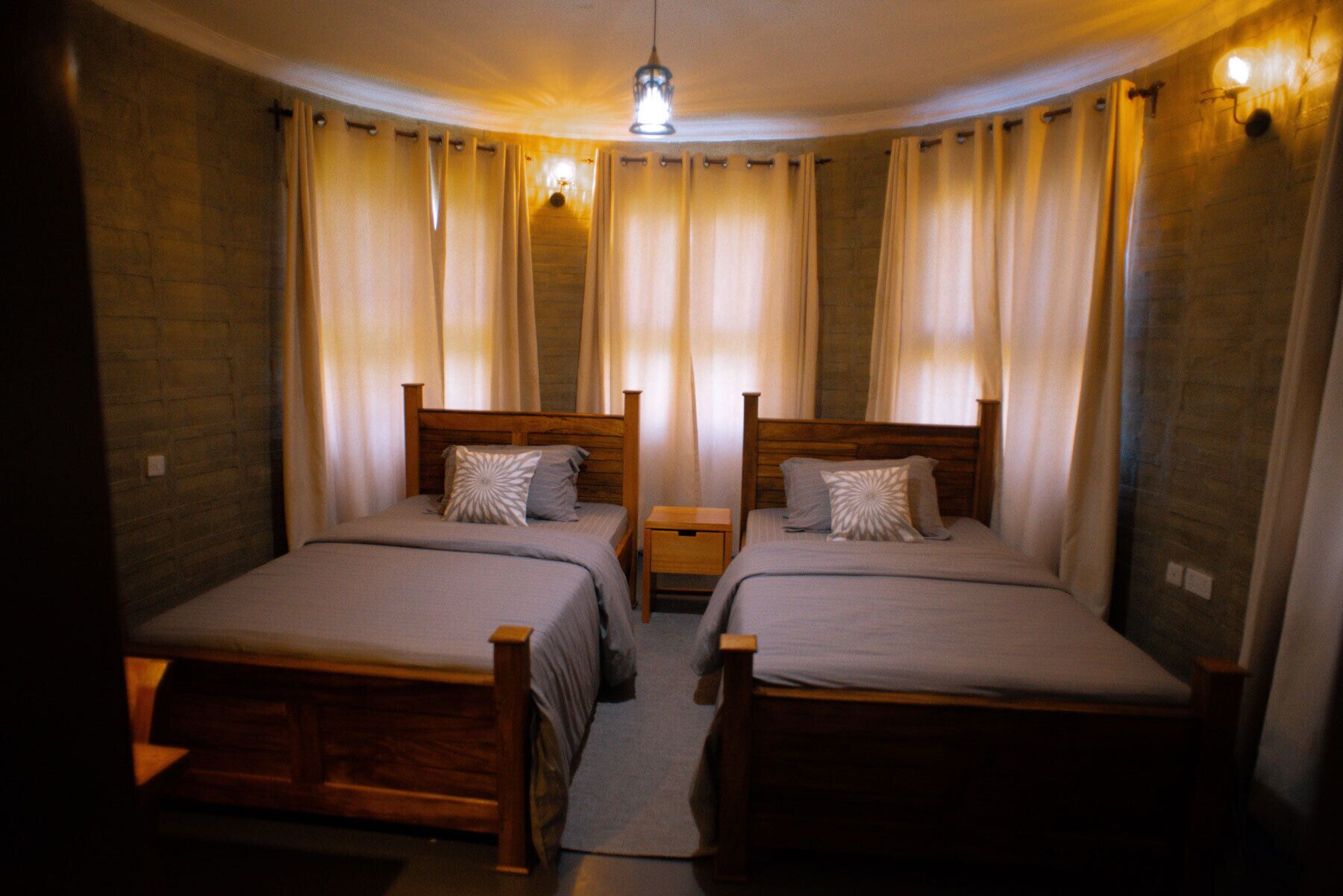 A room with two wooden beds, a nightstand, and a hanging light fixture.