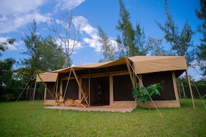 A tent with a simple, open design, surrounded by grass and trees.
