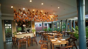 Ein Restaurant mit Holztischen und -stühlen, hängenden Terrakotta-Lampen und einer Ziegelwand.