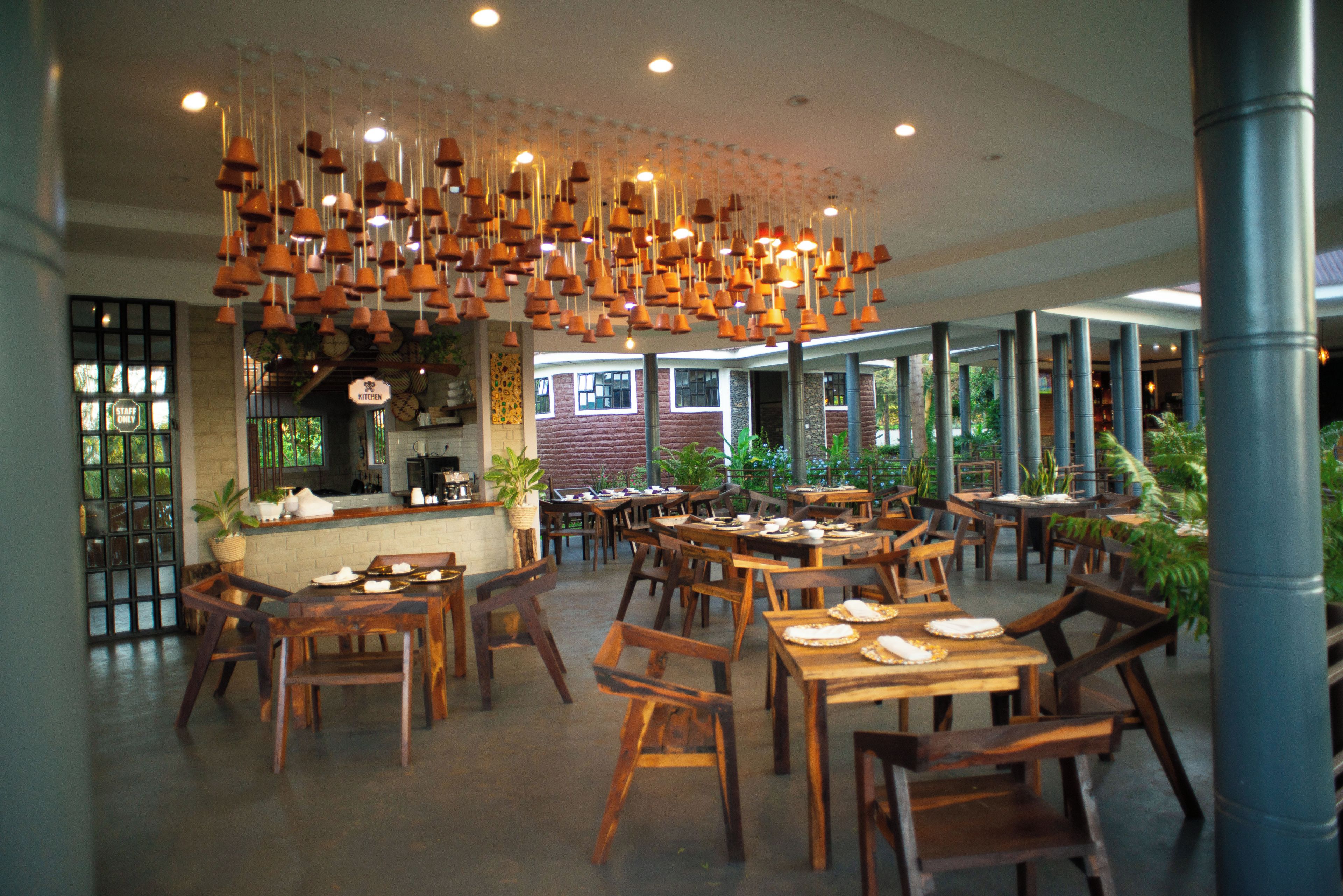 L’intérieur d’un restaurant, avec des tables et des chaises en bois, des luminaires suspendus et un espace cuisine.