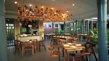 L’intérieur d’un restaurant, avec des tables et des chaises en bois, des luminaires suspendus et un espace cuisine.