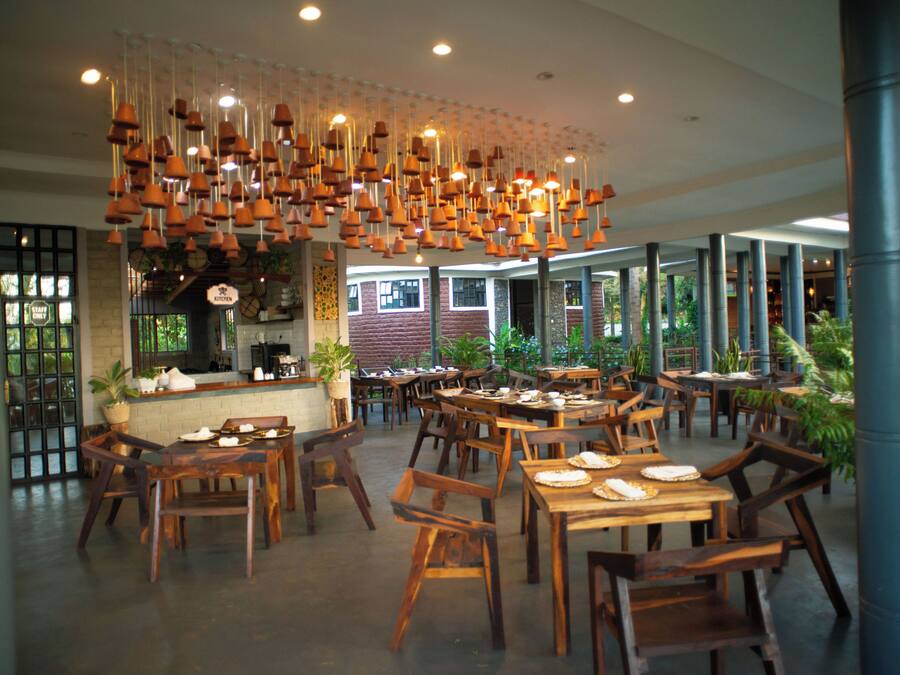 Un interior de restaurante con mesas y sillas de madera, lámparas colgantes y una zona de cocina.
