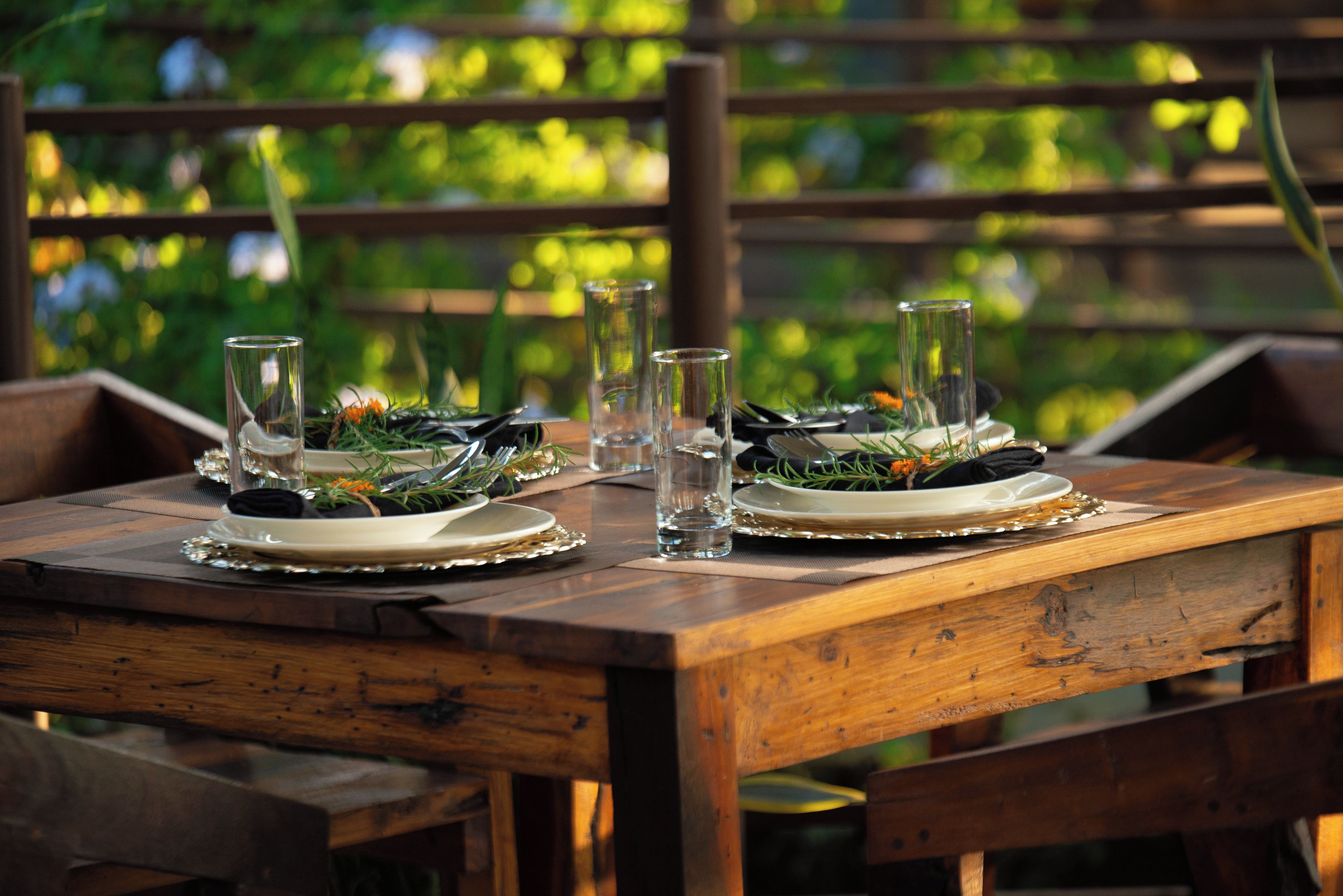 Une table de salle à manger en bois, mise avec des assiettes, des verres et des couverts, entourée de chaises.