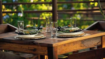 Une table de salle à manger en bois, mise avec des assiettes, des verres et des couverts, entourée de chaises.