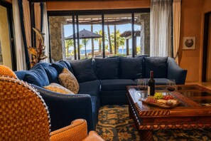 Ein modernes Wohnzimmer mit einer großen Eckcouch, einem Couchtisch mit Snacks und Blick auf Palmen und den Ozean.