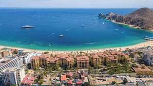 Un hotel frente al mar con varias construcciones, una playa y barcos en el agua.