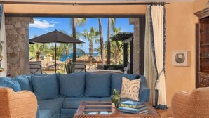 Un salón con un sofá azul, una mesa de centro de madera y vistas a palmeras y una piscina.