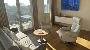 Ett modernt vardagsrum med en soffa, en fåtölj och ett soffbord. En tv är monterad på väggen och det finns ett fönster med gardiner.