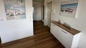 En hall med trägolv, vita väggar och två tavlor som föreställer måsar och en båt.