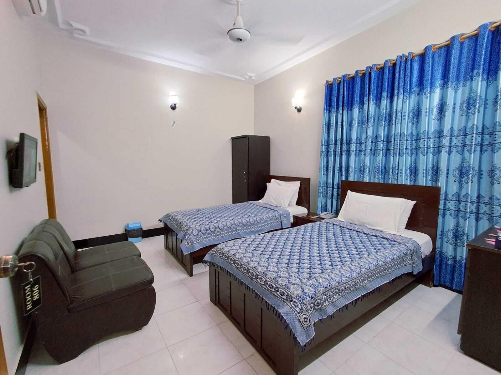 A hotel room with two single beds, a sofa, a cabinet, and a television.