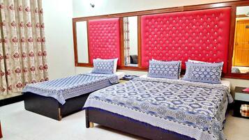 A hotel room with two beds, each with a patterned bedspread and pillows, a red upholstered headboard, and a mirror above the beds.