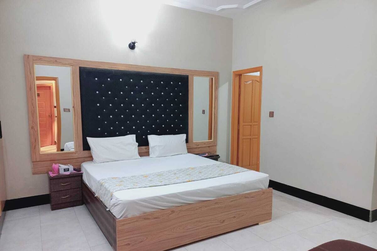 Quarto com uma cama grande, cabeceira de madeira, duas mesas de cabeceira, um espelho e um guarda-roupa.