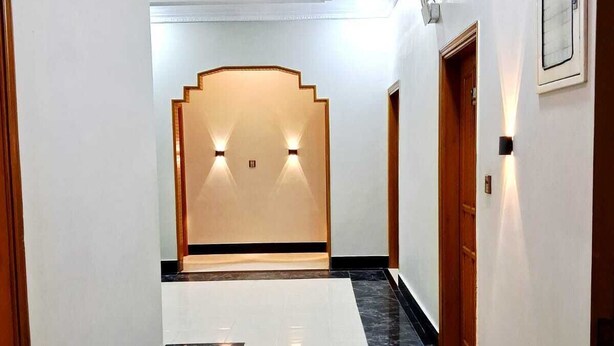 Un pasillo con suelo de mármol, paredes blancas y puertas de madera.
