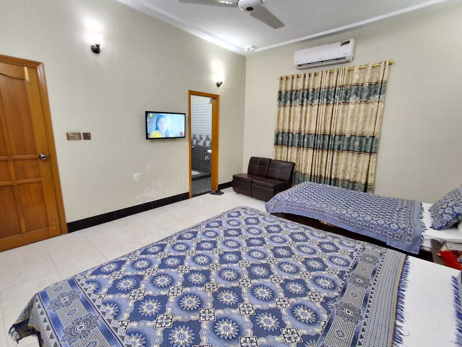 A bedroom with two beds, a TV, an air conditioner, and a window with curtains.