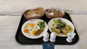 Una bandeja con dos platos de desayuno, que incluyen huevos, verduras y tostadas, además de dos cestas de pan.