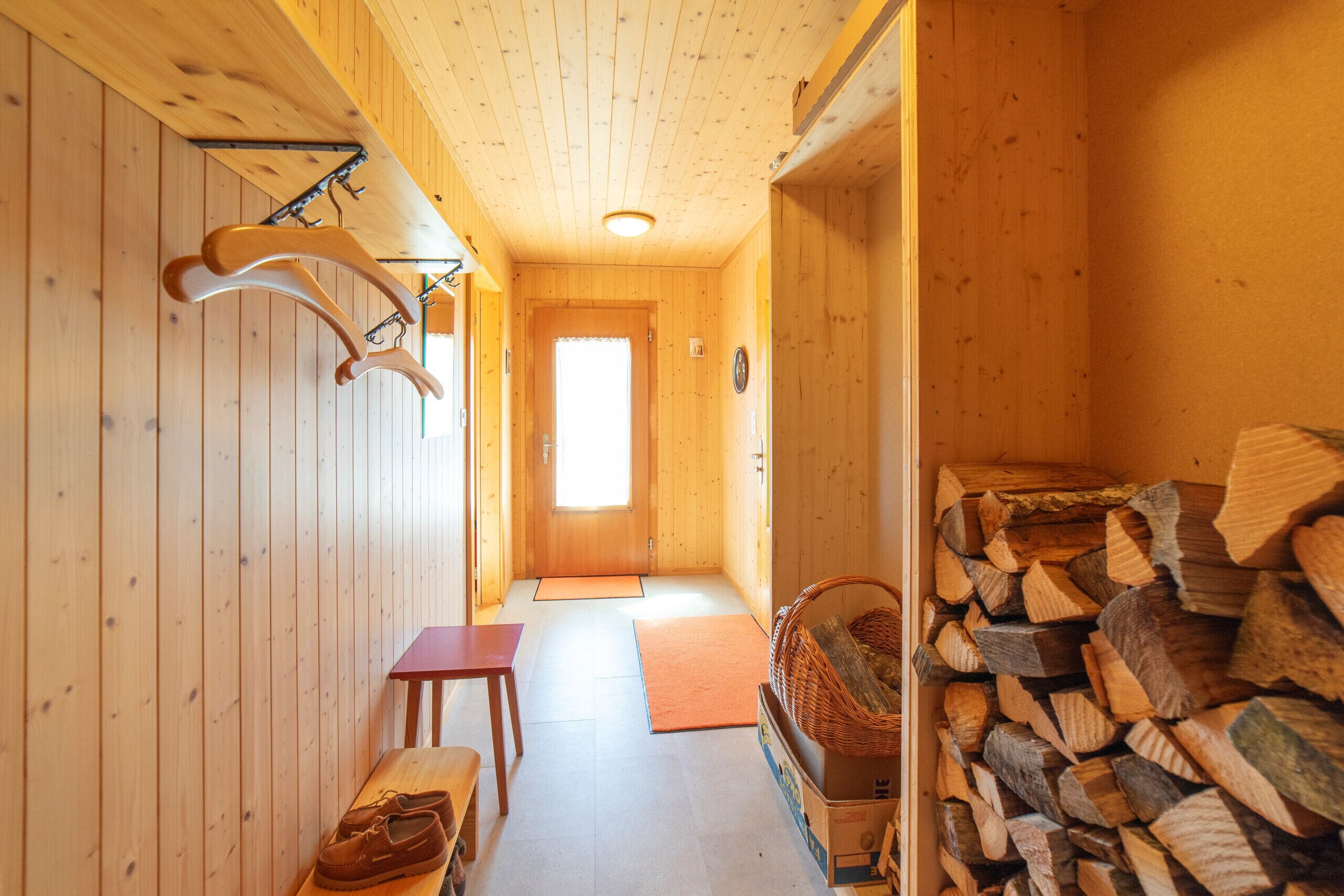 A wooden interior with a bench, a door, and a stack of firewood.