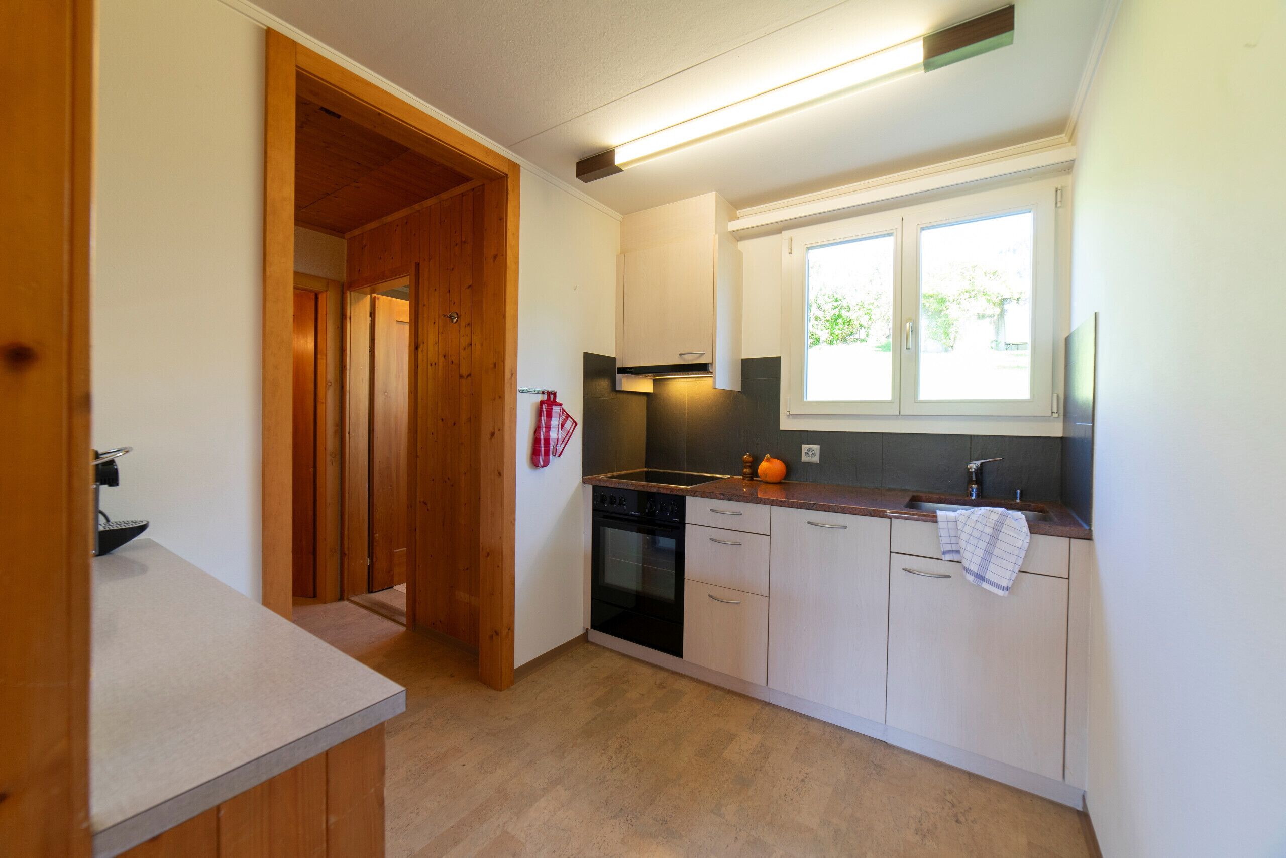 A compact kitchen with wooden cabinets, a built-in oven, and a window with a view of greenery.