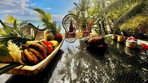 A tropical resort setting with a pool, wicker furniture, and a variety of fruits and flowers.