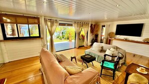 A spacious living room with a large window, a sofa, a coffee table, and a TV mounted on the wall.