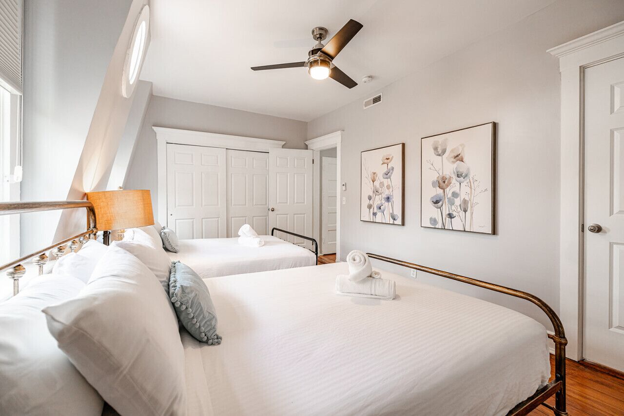 A hotel room with two beds, a ceiling fan, and artwork on the walls.