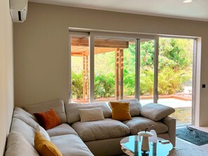 A modern living room with a sectional sofa, a glass coffee table, and a view of a garden through large sliding glass doors. - Apartment with Private Pool and Garden View (Saint-Martin)