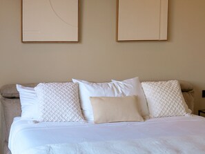A bed with white bedding and multiple pillows, a beige wall, and two framed pictures above the bed. - Apartment with Private Pool and Garden View (Saint-Martin)