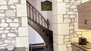 Uma cozinha com parede de pedra, escada de madeira e bancada com torradeira.