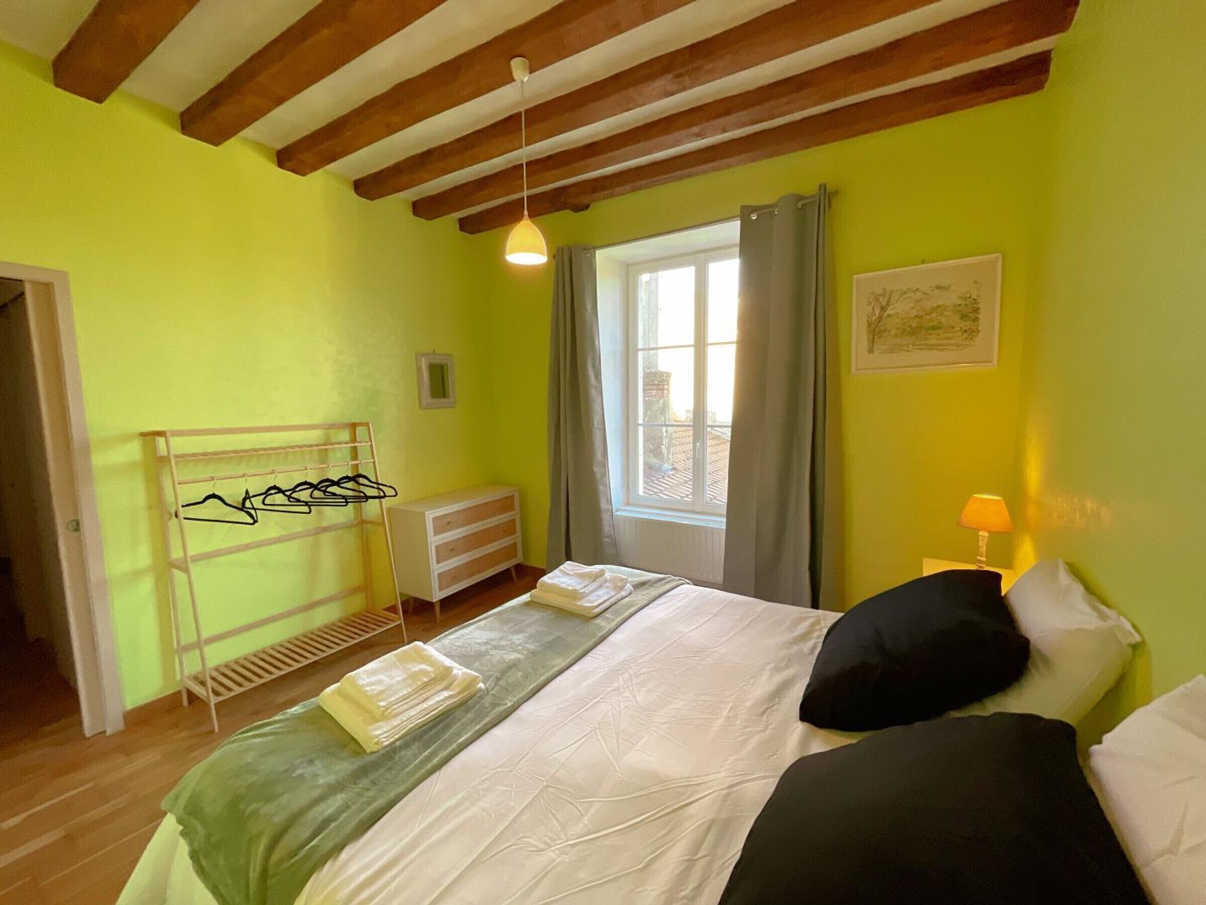A bedroom with a bed, a radiator, a window with curtains, a hanging clothes rack, and a lamp.