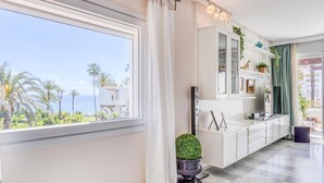 A modern kitchen with a large window, white cabinetry, and a view of palm trees and the sea.