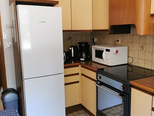 A compact kitchen with a white Bosch refrigerator, a microwave, a coffee maker, and a small oven.