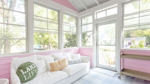 A white sofa with multiple pillows, including one with "LAKE LIFE" text, in a room with large windows and a pink wall. - Designer Downtown Home, Assn Pool, Walk To Beach (New Buffalo)