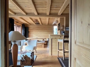 Interior de madeira com área de jantar, bar e espaço de estar com uma luminária e um objeto decorativo.