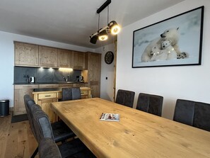 A modern kitchen with wooden cabinets, a dining area with a wooden table and chairs, and a framed polar bear picture on the wall.